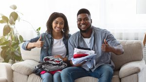 A picture of a smiling Black couple, holding clothes for donation in their laps as they each give a thumbs-up